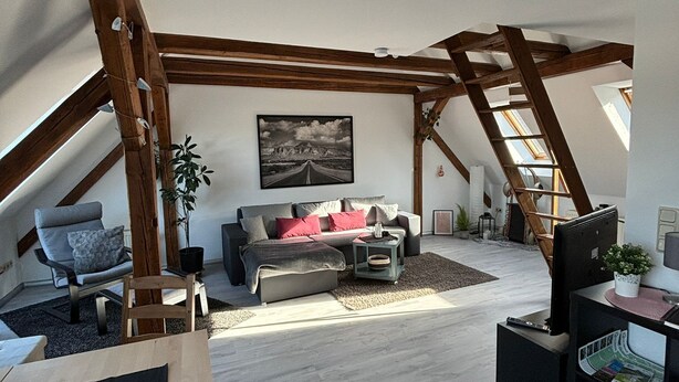 An attic room with a loft bed, a sofa, a desk, and a window.