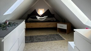A small, triangular attic bedroom with a bed, a nightstand, and a dresser.