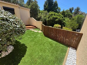 A landscaped garden with artificial grass, a wooden deck, and a bamboo fence.
