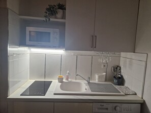 A kitchen with a microwave, a sink, a dishwasher, and a countertop with a kettle, a sponge, and a bottle.