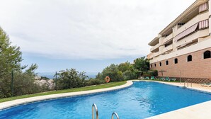 Una piscina con borde curvo, rodeada por un muro bajo y un edificio con varios balcones.
