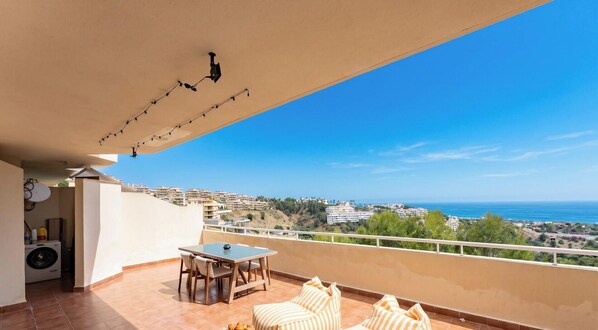 A balcony with a table and chairs, a washing machine, and a view of the sea and buildings. - Relaxing Sea View Escape in Calahonda (Mijas Costa)