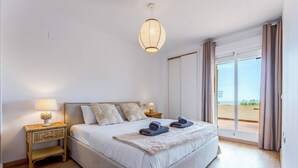 Un dormitorio con cama, lámparas de noche, vistas por una ventana y un balcón.