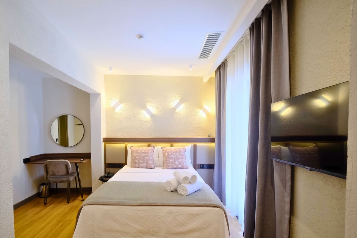 A hotel room with a bed, a desk, a chair, a TV, and a mirror.