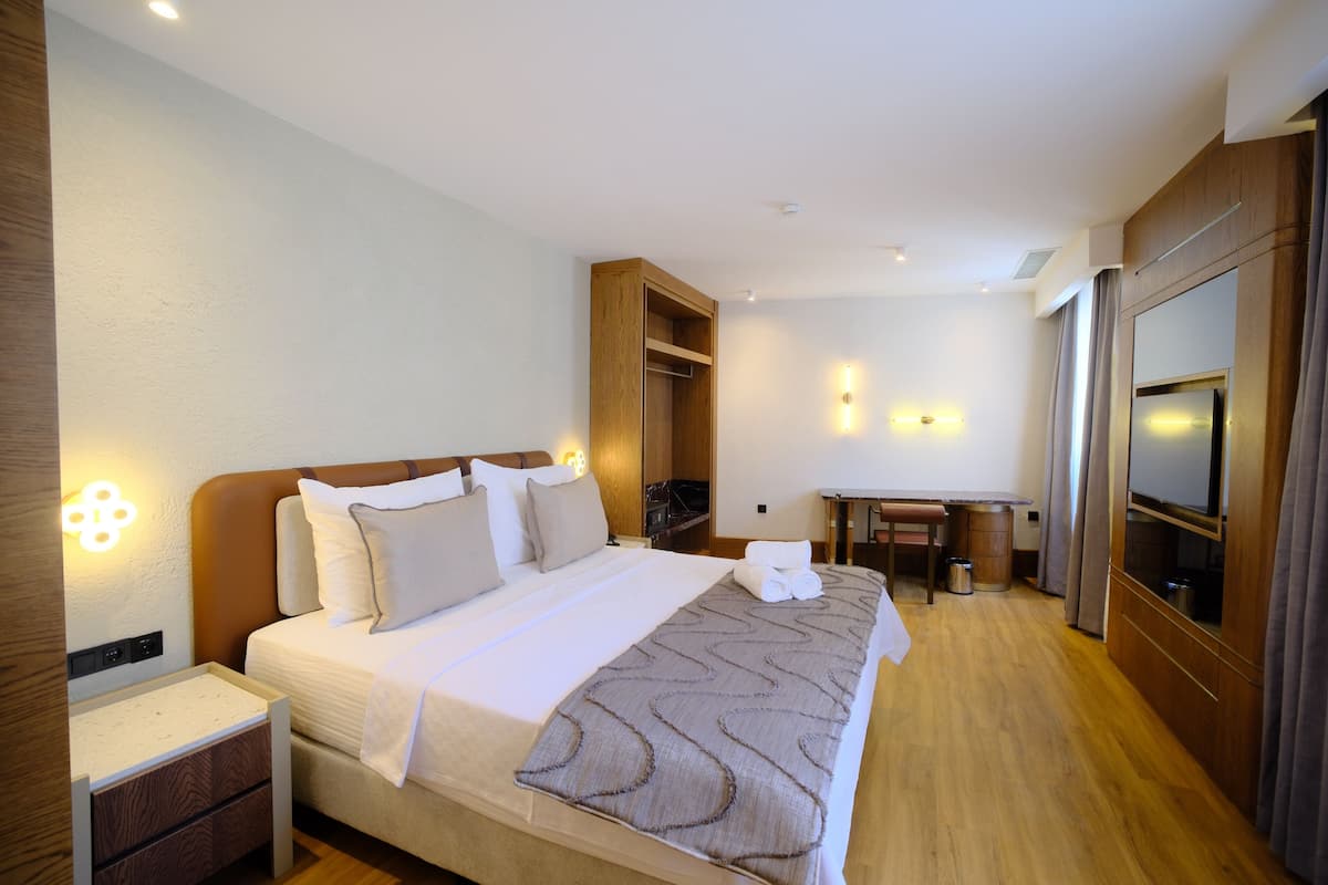 A hotel room with a bed, bedside tables, a desk, a mirror, and a wardrobe.