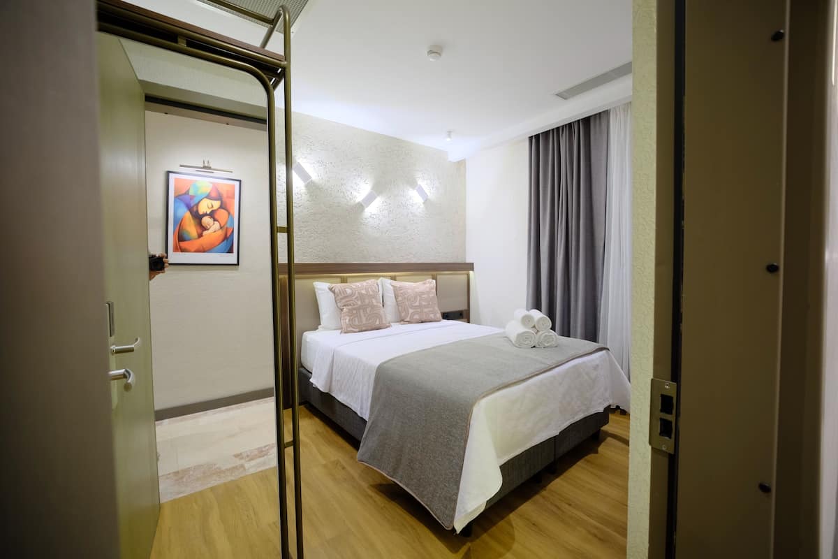 A hotel room with a bed, pillows, a painting, and a curtain.