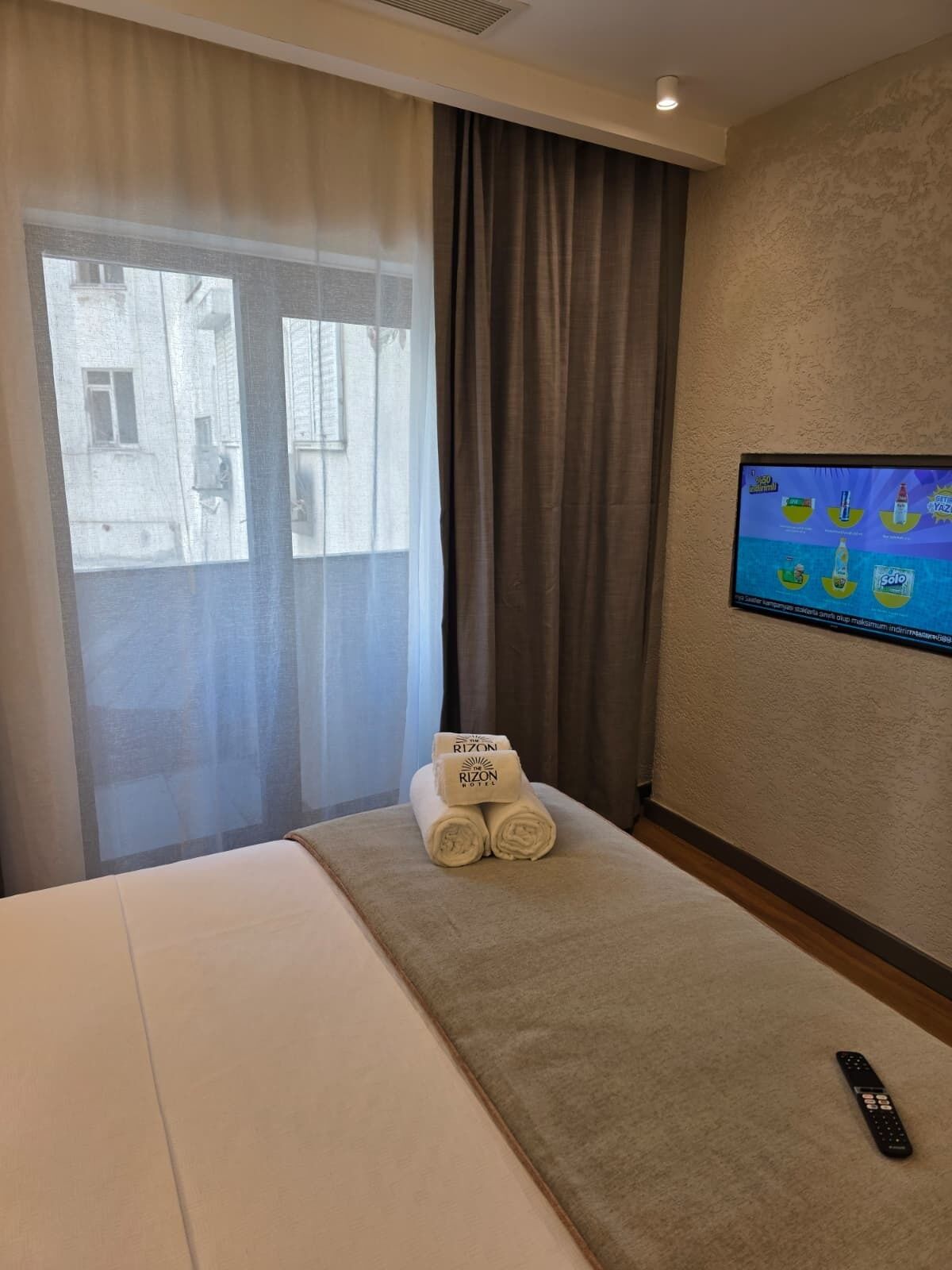 A hotel room with a bed, a TV on the wall, and a window with curtains.
