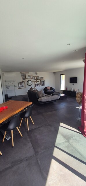 A modern living room with a dining table, sofa, and a flat-screen TV mounted on the wall. - Comfortable villa at the gateway to the gorges (Vinon-sur-Verdon)