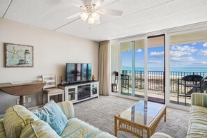 Ein Wohnzimmer mit Fernseher, einer Couch und Blick auf den Strand durch große Schiebeglastüren.