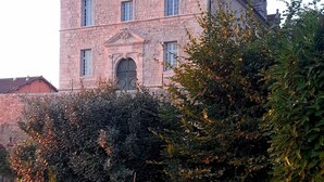 Ein großes Steinhaus mit mehreren Schornsteinen, einem zentralen Eingang und einem umlaufenden Garten mit verschiedenen Pflanzen und Blumen.