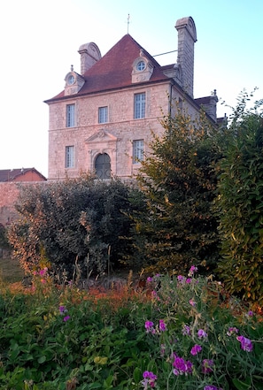 A large stone building with multiple chimneys, a central entrance, and a surrounding garden with various plants and flowers. - Beautiful South Burgundy: airy, spacious house with views, nature sports, (Saint-Bonnet-de-Joux)