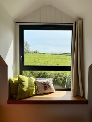A room with a window overlooking a green field, a wooden bench with cushions, and a white wall. - Beautiful South Burgundy: airy, spacious house with views, nature sports, (Saint-Bonnet-de-Joux)