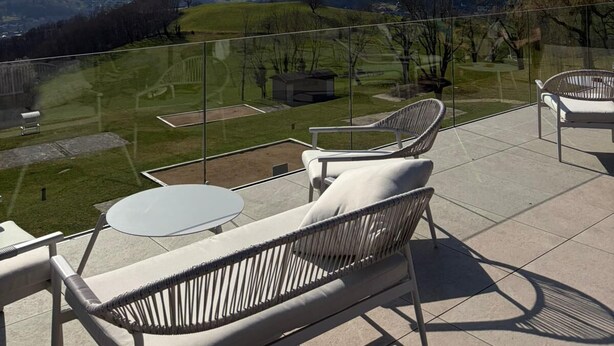 Una terraza con mobiliario exterior, baranda de vidrio y vistas a colinas ondulantes y montañas.