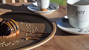Una mesa con un tablero de ajedrez, una taza, un platito y un plato con un postre.