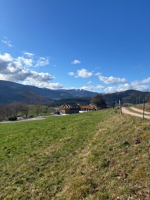 A rural landscape with a house on a hill, a dirt path, and mountains in the background. - Domaine Le H - A Destination at the Peak of Your Dreams (Hohrod)