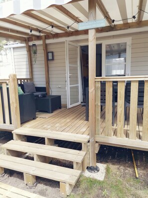 A wooden deck with a covered seating area, a wooden bench, and a sign with text. - Charming mobile home with all comforts (Saint-Julien-en-Born)