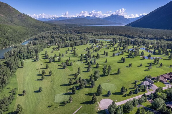 A golf course with a lake, mountains, and a clear sky.