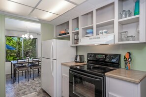 A kitchen with a refrigerator, oven, and a dining area with chairs and a table.