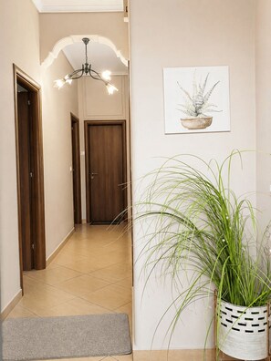 A hallway with wooden doors, a tiled floor, a grey rug, a hanging plant, and a framed plant illustration on the wall. - Sandy’s House – Peaceful Stay in Gymno, Evia (Gimno)