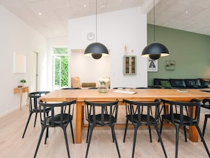 A dining area with a wooden table and black chairs, a green wall with a sofa, and a clock on the wall. - 5 Star Holiday Home in Farvang (Farvang)