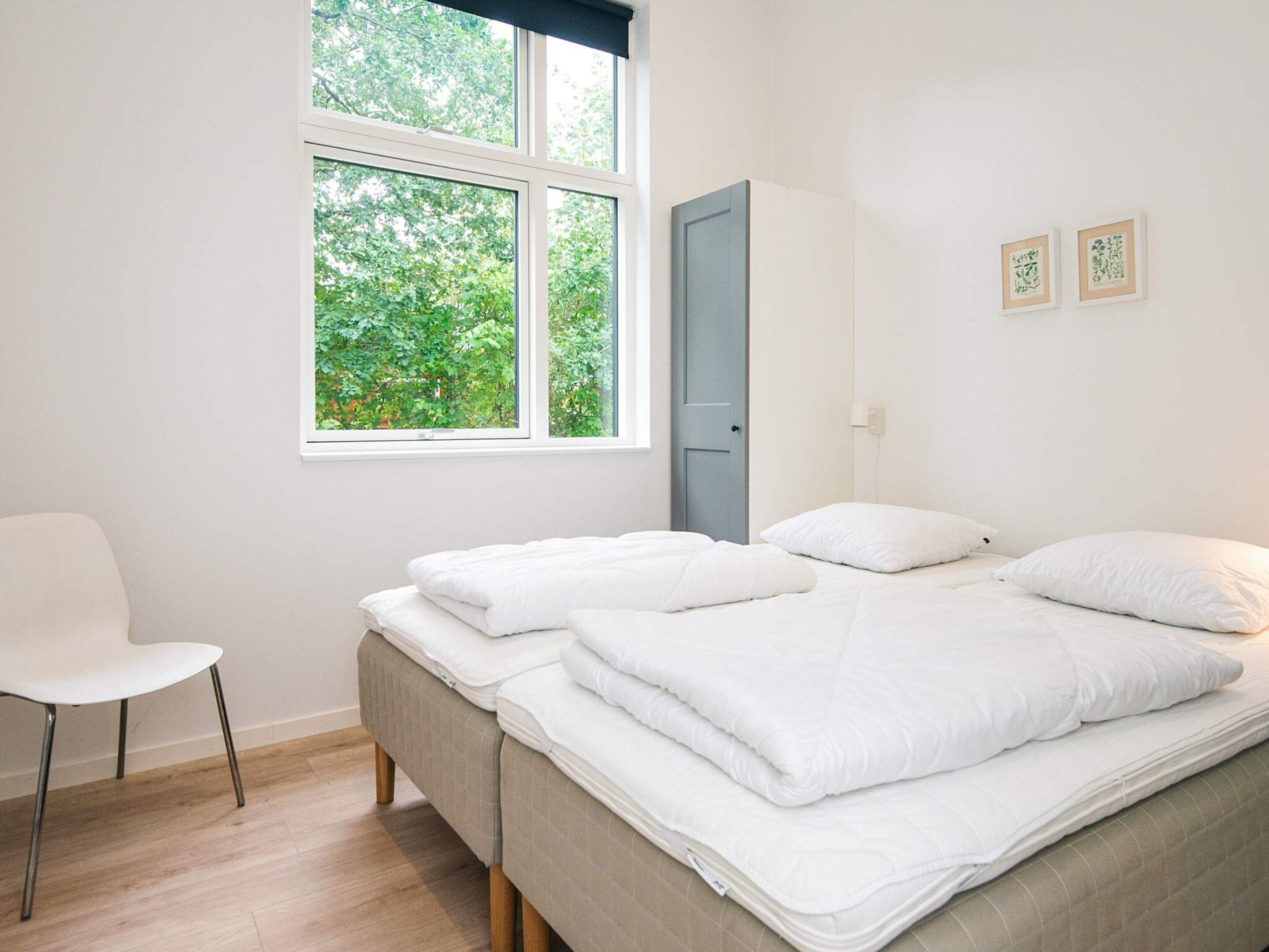 A bedroom with a bed, a chair, a wardrobe, and a window with a view of trees.