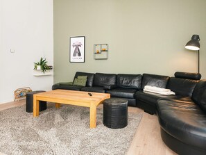 A modern living room with a black leather sofa, a wooden coffee table, and a small side table. - 5 Star Holiday Home in Farvang (Farvang)