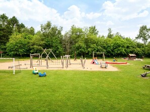 Ein Spielplatz mit Schaukeln, Rutschen und einem kleinen Gebäude.