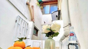 Un espacio exterior reducido con una mesa dispuesta para una comida, con naranjas, una taza y una botella.