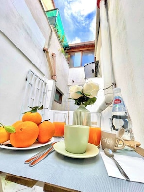 A narrow outdoor space with a table set for a meal, including oranges, a coffee cup, and a bottle of water. - Cozy Apartment in the Heart of the City (Palermo)