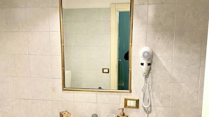 Un baño con lavamanos blanco, espejo, secador de pelo y toallero.