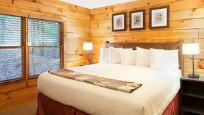 A wooden-paneled room with a large bed, two bedside lamps, and framed pictures on the wall.