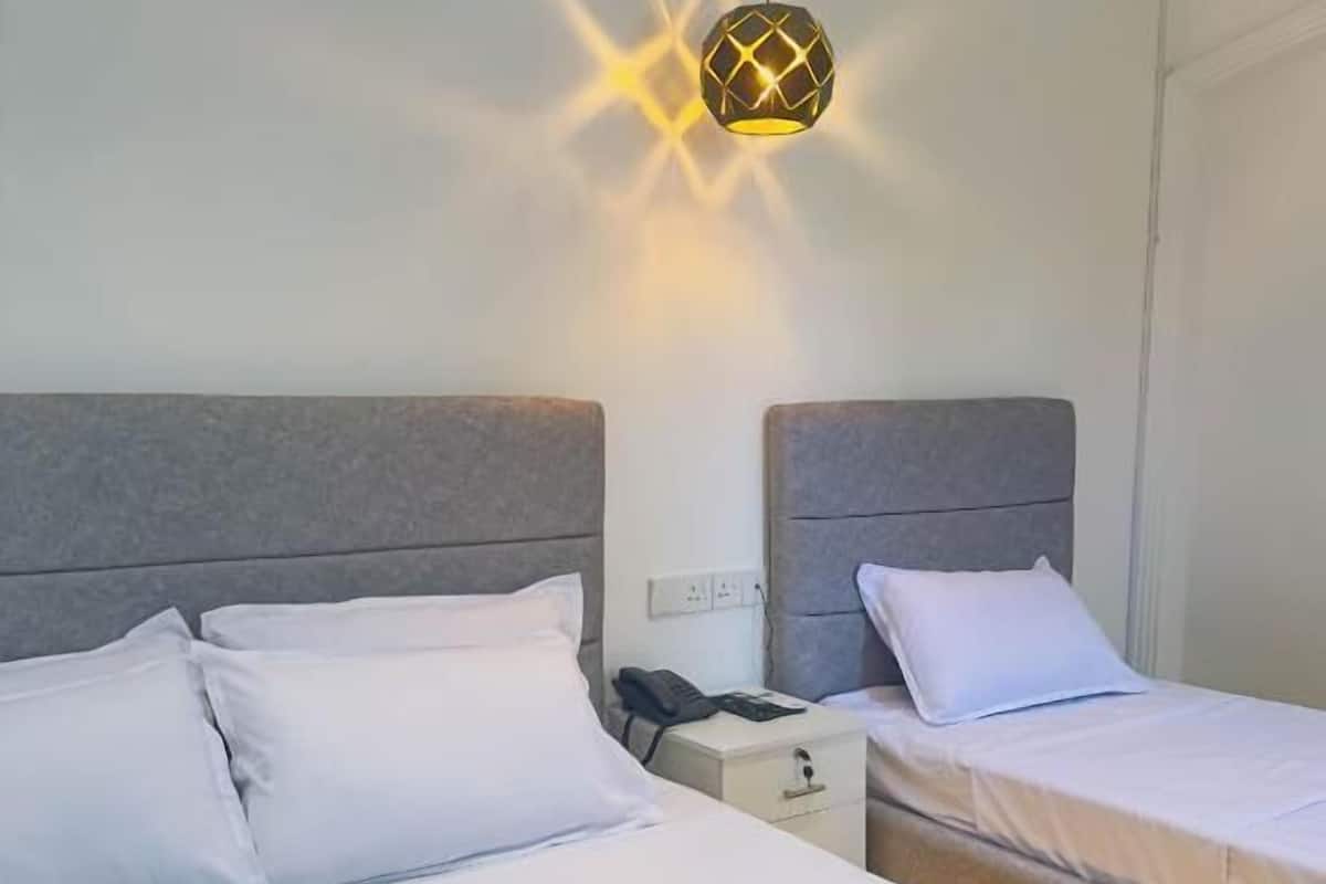 Quarto de hotel com duas camas, uma mesa de cabeceira com telefone e uma luminária.