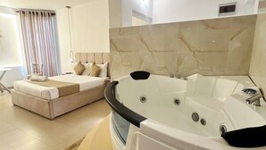 A modern bathroom with a large bathtub, a sofa, and a window with curtains. - La Costa Hotel (Seeduwa)