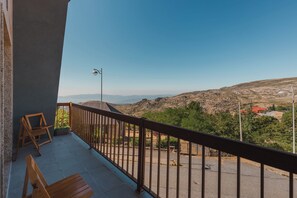 Ein Balkon mit Blick auf eine hügelige Landschaft, eine Straßenlaterne und ein Gebäude mit rotem Dach in der Ferne.