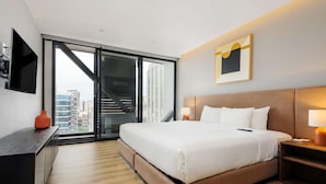 Camera d'albergo moderna con un letto grande, una scrivania, una televisione e vista sulla città attraverso una porta scorrevole.
