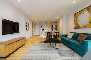 Ein modernes Wohnzimmer mit Fernseher, Sofa, Couchtisch und einer Küche im Hintergrund.