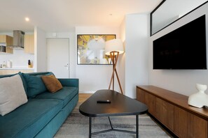A modern living room with a teal sofa, a coffee table, a lamp, and a flat-screen TV mounted on the wall. - w Charming 1BR w/ AC in the Heart of Roma Sur (Mexico City)