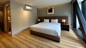 Una moderna camera d'hotel con un letto grande, comodini, condizionatore d'aria a parete e una finestra con vista.