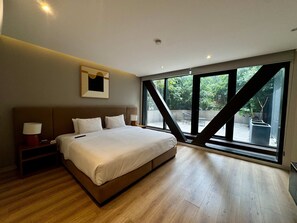 Ein modernes Schlafzimmer mit einem großen Bett, Nachttischlampen, einem gerahmten Bild und Blick durch große Fenster.