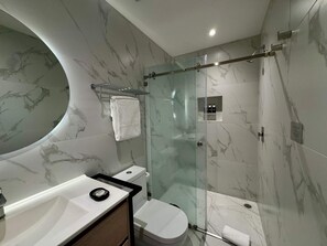 Ein modernes Badezimmer mit Duschkabine aus Glas, weißer Toilette und Waschtisch mit Marmorplatten.