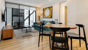 Una sala de estar moderna con un sofá, una mesa de comedor con sillas, una escalera y un ventanal grande.