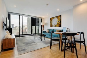 Ein modernes Wohnzimmer mit einer Couch, einem Esstisch und Stühlen, einem großen Fenster mit Blick auf die Stadt sowie einem Bild an der Wand.