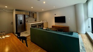 A modern kitchen with a built-in refrigerator, microwave, and stove. There is a dining area with a wooden table and chairs, and a green sofa with cushions. A flat-screen TV is mounted on the wall. - w Pleasant 1BR w AC in the Heart of Roma Sur (Mexico City)