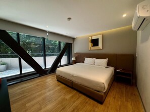 Ein modernes Hotelzimmer mit einem großen Bett, einem Nachttisch, einem wandmontierten Spiegel und einem Fenster mit Blick auf Grünflächen.