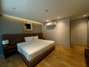 Ein modernes Hotelzimmer mit Bett, Nachttisch, Wandairconditioner und einer Tür.