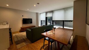 A modern living space with a wooden dining table, a green sofa, a flat-screen TV, and a kitchen area with a sink. - w Pleasant 1BR w AC in the Heart of Roma Sur (Mexico City)