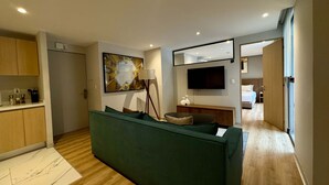 A modern living room with a green sofa, a flat-screen TV, a painting, and a kitchen area with wooden cabinets. - w Appealing 1BR w AC in the Heart of Roma Sur (Mexico City)