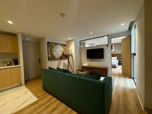 A modern living room with a green sofa, a flat-screen TV, a painting, and a kitchen area with wooden cabinets. - w Appealing 1BR w AC in the Heart of Roma Sur (Mexico City)
