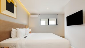 A hotel room with a bed, bedside table, lamp, air conditioning unit, window, and a mounted TV. - w Deluxe 1BR w/ AC in the Heart of Roma Sur (Mexico City)