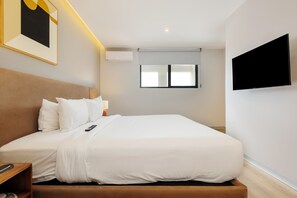 A hotel room with a bed, bedside table, lamp, air conditioning unit, window, and a mounted TV. - w Deluxe 1BR w/ AC in the Heart of Roma Sur (Mexico City)
